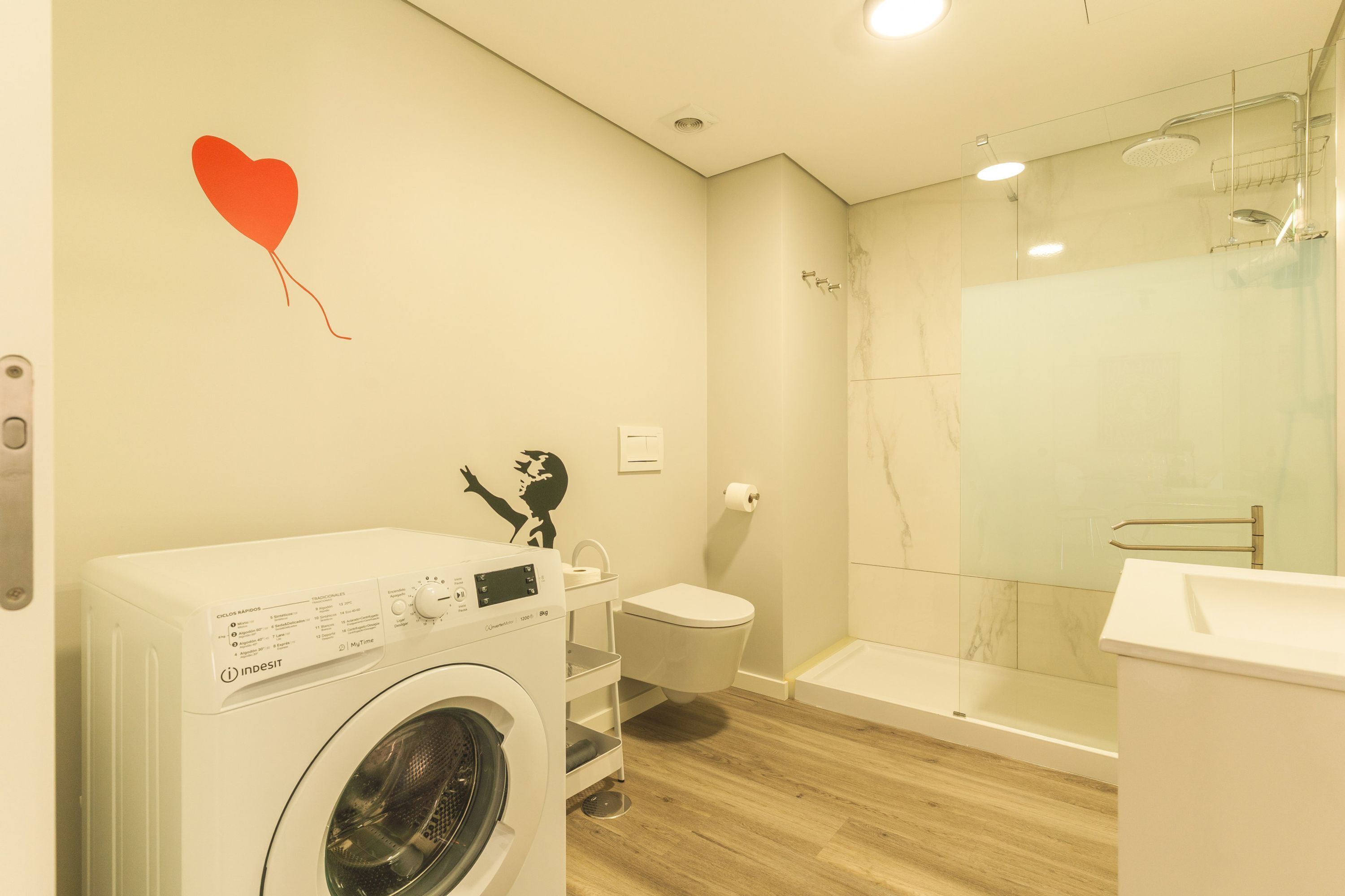 A modern bathroom with a washing machine, toilet, and glass shower enclosure.