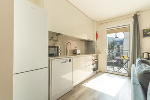 Une cuisine compacte équipée d’un lave-vaisselle, d’un four à micro-ondes et d’un four traditionnel, donnant sur un balcon avec vue sur la ville.