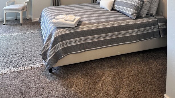 A bedroom with a bed, a chair, a ceiling light, and a wall-mounted mirror.