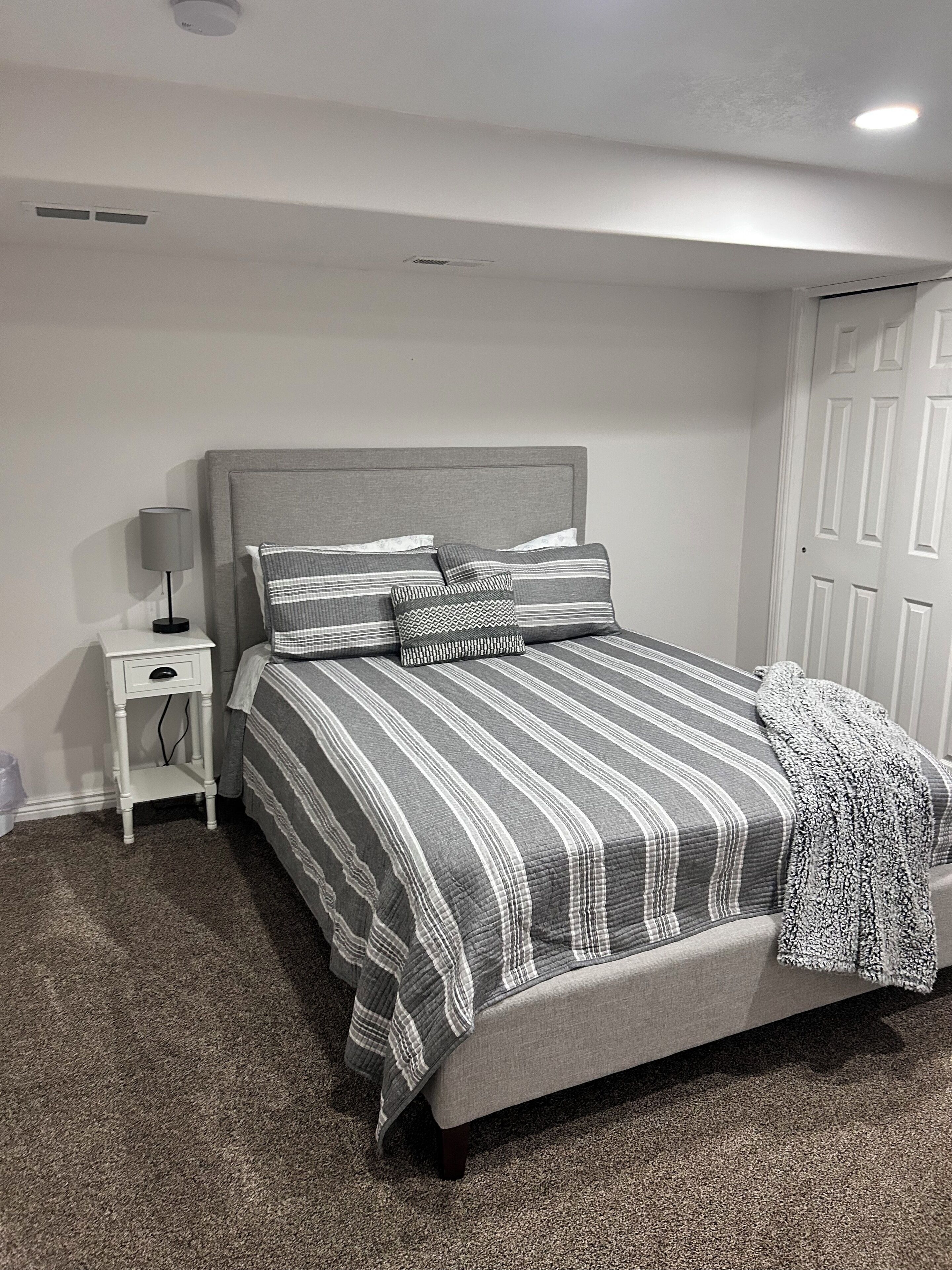 Ein Schlafzimmer mit einem Bett, einem Nachttisch, einer Lampe und einer Tür.
