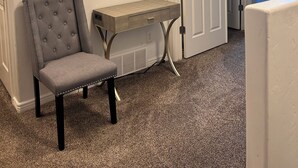 A room with a grey tufted chair, a wooden desk, and a white door leading to another room.
