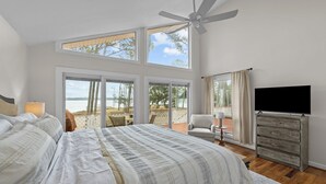Ein Schlafzimmer mit einem großen Bett, einem Deckenventilator, einem Fernseher und einem Balkon mit Meerblick.