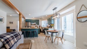 A modern kitchen with teal cabinets, a central island, and a dining area with a round table and chairs. - Cute modern 2 bed retreat, a perfect basecamp for your adventures! (Fraser)