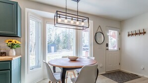 A dining area with a round table, four chairs, a hanging light fixture, and a view through large windows. - Cute modern 2 bed retreat, a perfect basecamp for your adventures! (Fraser)
