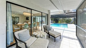 A covered outdoor area with a pool, seating, and a dining area visible through glass doors.