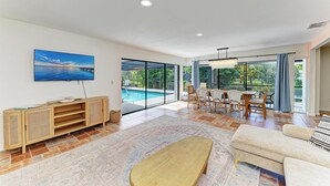 A spacious living area with a large window, a pool, and a dining set.