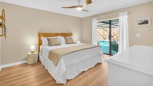 A bedroom with a bed, a ceiling fan, a nightstand, and a view of a pool through a glass door.