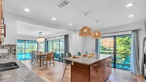 A modern kitchen with a large island, dining area, and a view of a swimming pool.