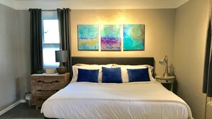Ett hotellrum med en säng, sängbord, en lampa, en klocka och abstrakt konst på väggen.