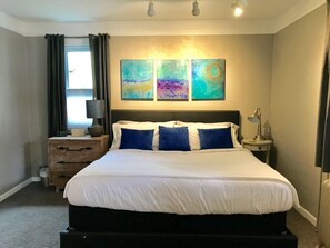A hotel room with a bed, bedside tables, a lamp, a clock, and abstract wall art. - The Tranquil Farmhouse is a 2-bedroom house in the Kerrytown Historic District  (Ann Arbor)