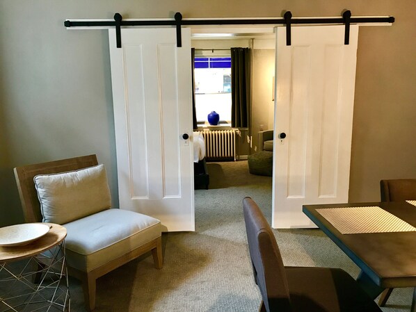 A room with a sliding door, a sofa, a small round table, and a dining table.