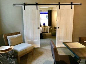 A room with a sliding door, a sofa, a small round table, and a dining table.