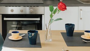 A dining area with a table set for two, featuring a vase with a single red rose, two cups, and a pair of chopsticks.