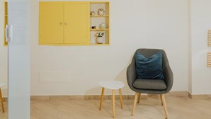 A modern room with a wooden ceiling, a yellow cabinet with shelves, a grey armchair with a blue cushion, and a small white table.