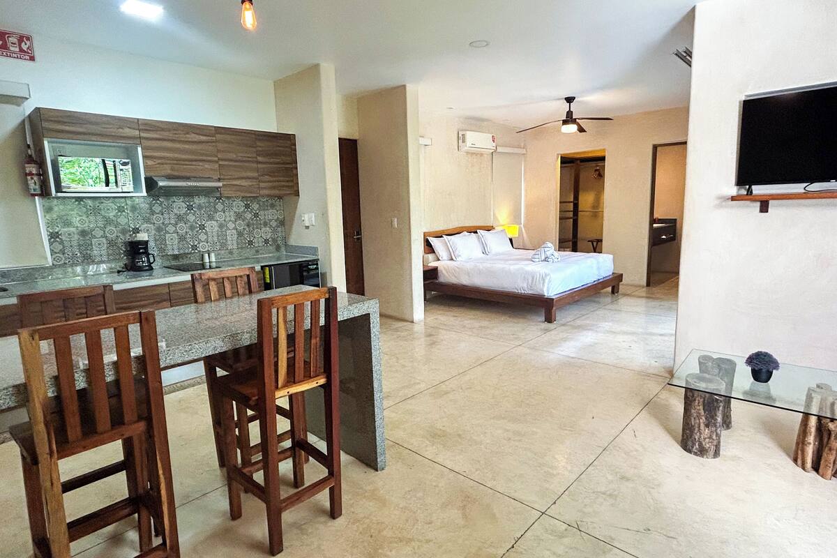 A modern hotel room with a kitchen area, a dining space, and a bedroom.