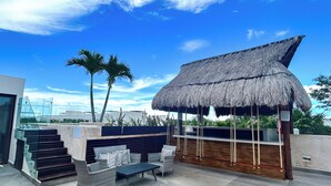 A rooftop terrace with a thatched roof structure, outdoor seating, and palm trees. - Albra Tulum (Tulum)
