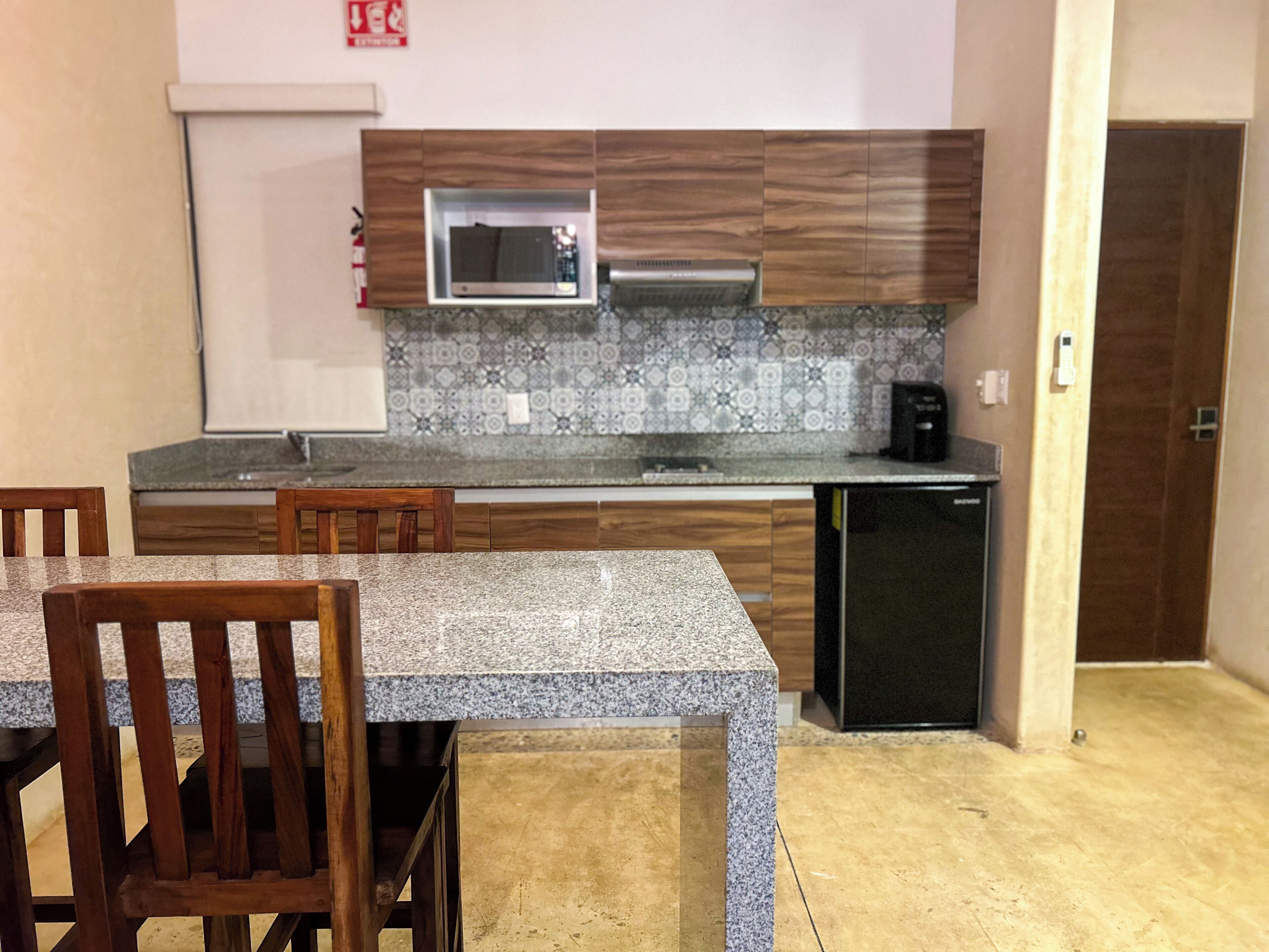 A compact kitchen with wooden cabinets, a microwave, a coffee maker, and a small refrigerator.