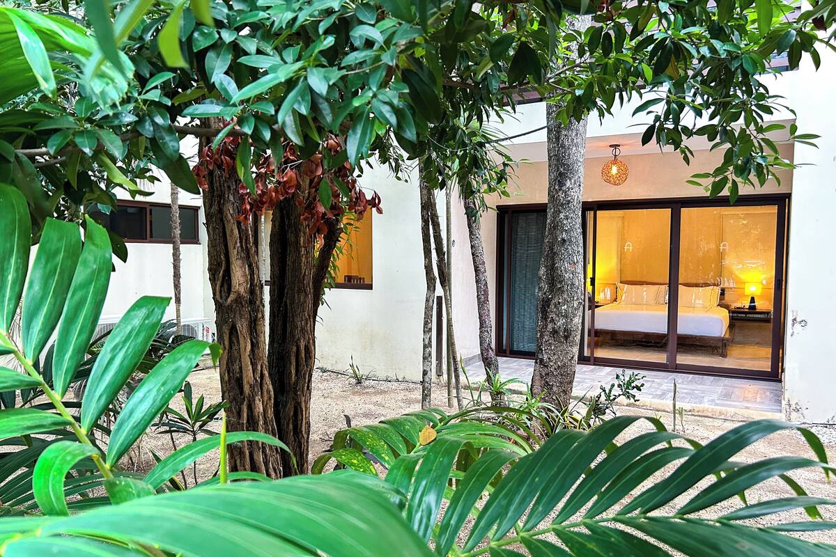 A modern hotel with a large glass room, a well-maintained garden, and a clear view of the interior.