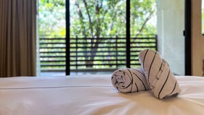 A neatly made bed with a rolled towel, a view of a balcony with a wooden fence, and a door leading outside. - Albra Tulum (Tulum)