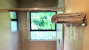 A bathroom with a towel rack holding a folded towel, a window with a view of greenery, and wooden flooring. - Albra Tulum (Tulum)