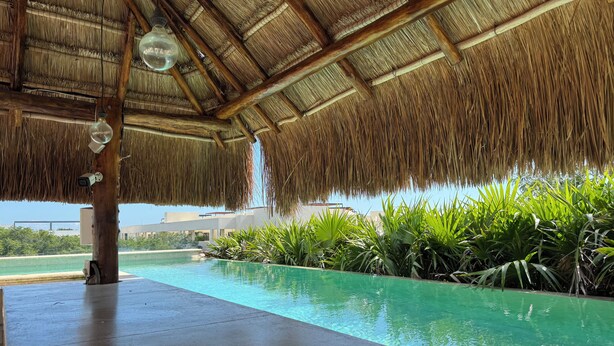 A pool area with a thatched roof, surrounded by lush greenery. - Albra Tulum (Tulum)