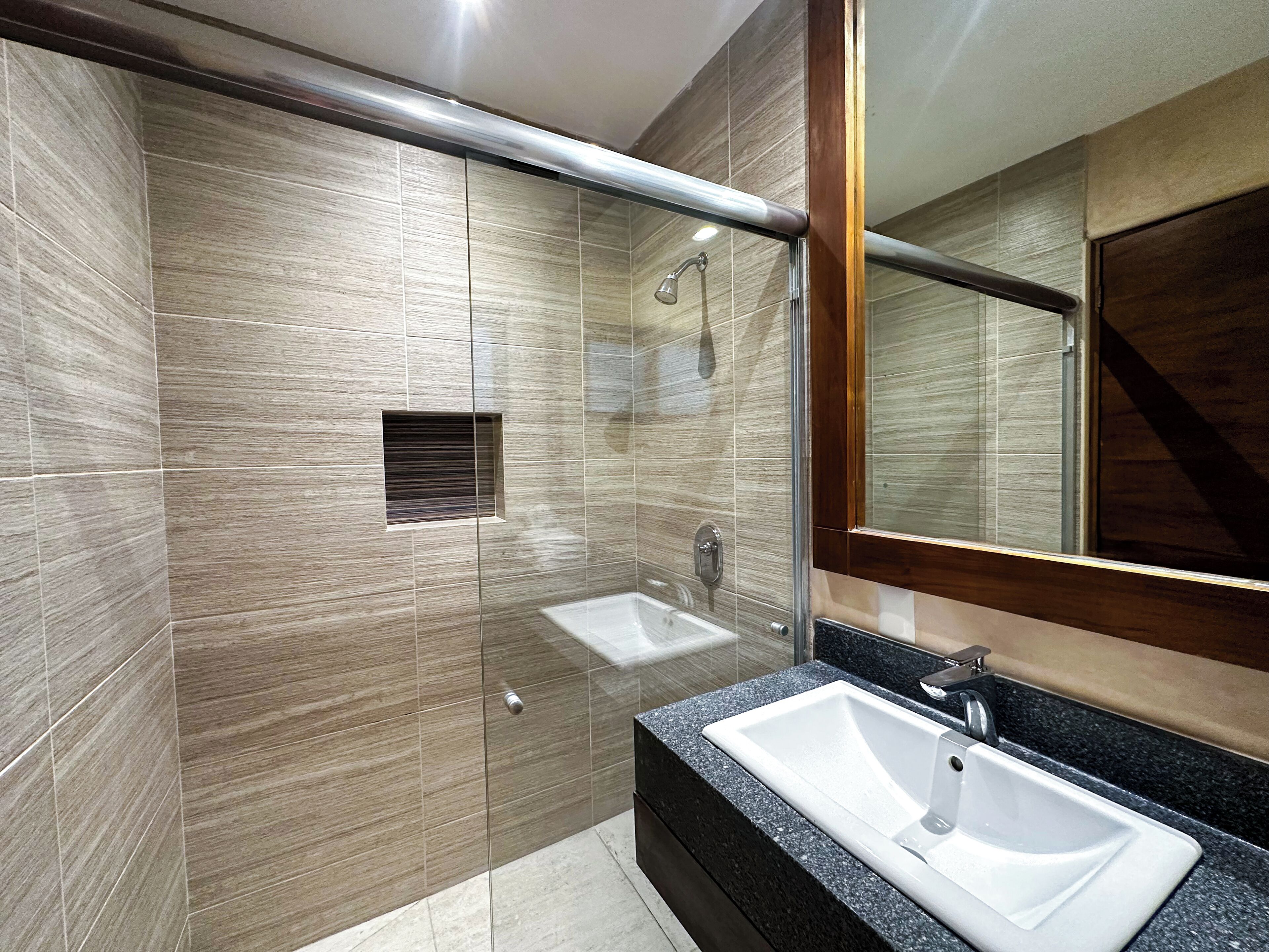 A modern bathroom with a glass-enclosed shower, a large mirror, and a granite countertop with a sink.