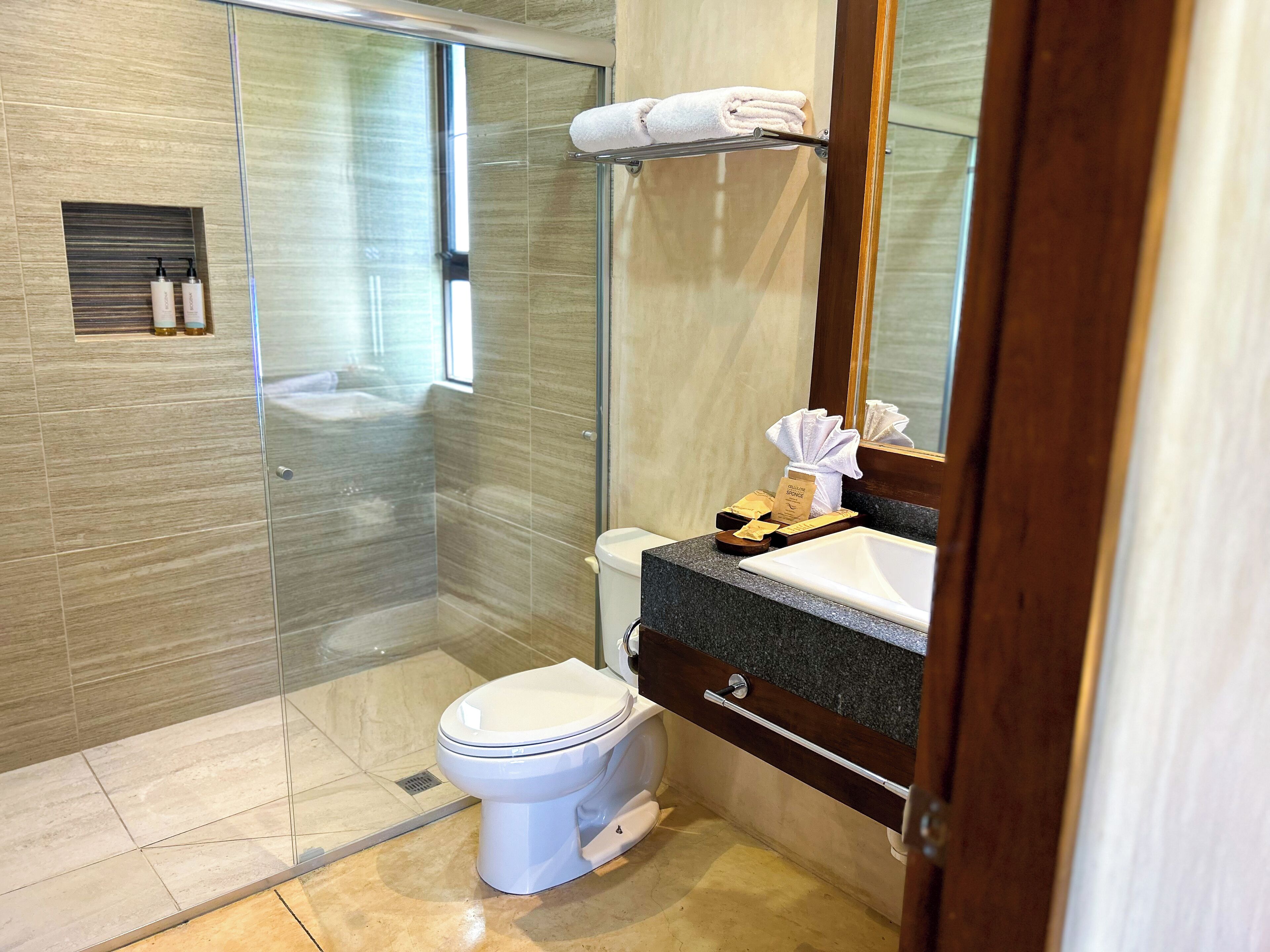 Une salle de bain moderne avec une douche à parois de verre, des toilettes blanches et un comptoir en granit doté d’un lavabo et d’un miroir.