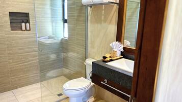 Une salle de bain moderne avec une douche à parois de verre, des toilettes blanches et un comptoir en granit doté d’un lavabo et d’un miroir.