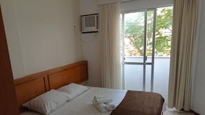 Een hotelkamer met een bed, een houten hoofdeinde, een raam met gordijnen en uitzicht op groen.
