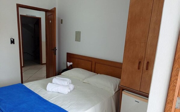 Een hotelkamer met een bed, een kledingkast, een kleine koelkast en een deur die naar een andere kamer leidt.
