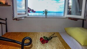 Ett rum med en säng, ett bord med en ros och ett fönster med utsikt över havet.