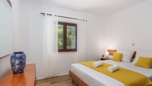 Ein Schlafzimmer mit einem Bett, einem Nachttisch, einer Lampe, einem Fenster mit Vorhängen und einer Vase auf einem Tisch.