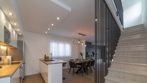 A modern kitchen with a central island, dining area with chairs, and a staircase.