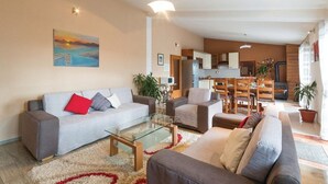 A modern living room with a sofa, armchairs, a glass coffee table, and a painting on the wall.