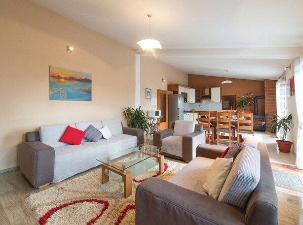A modern living room with a sofa, armchairs, a glass coffee table, and a painting on the wall.