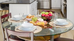 Una cocina moderna con una mesa de vidrio dispuesta para una comida, con platos, tazones y un frutero.