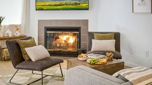Una sala de estar acogedora con chimenea, dos sillones, un sofá y una mesa de centro con aperitivos.