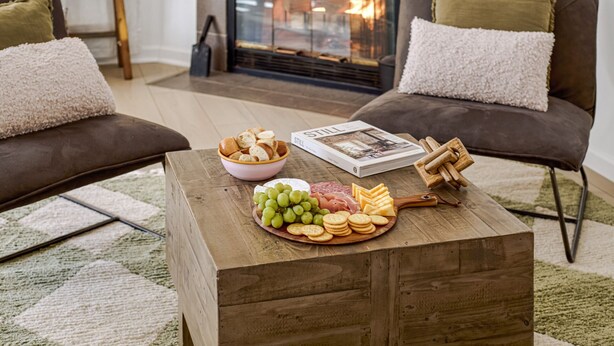 Un salón acogedor con chimenea, dos sofás, una mesa de centro con aperitivos y una revista.