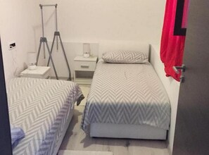 Two single beds with patterned bedspreads, a bedside table, and a lamp.