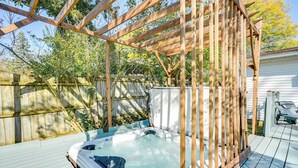 Un bain à remous sous une pergola en bois, dans un jardin avec une clôture en bois et une maison en arrière-plan.