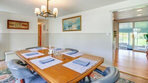 Une salle de conférence avec une table en bois, des chaises et des documents. On y trouve un lustre, un tableau et une porte qui donne sur une autre pièce.