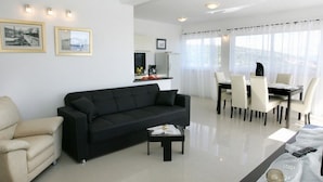 A modern living room with a black sofa, a beige armchair, and a dining area with a table and chairs.