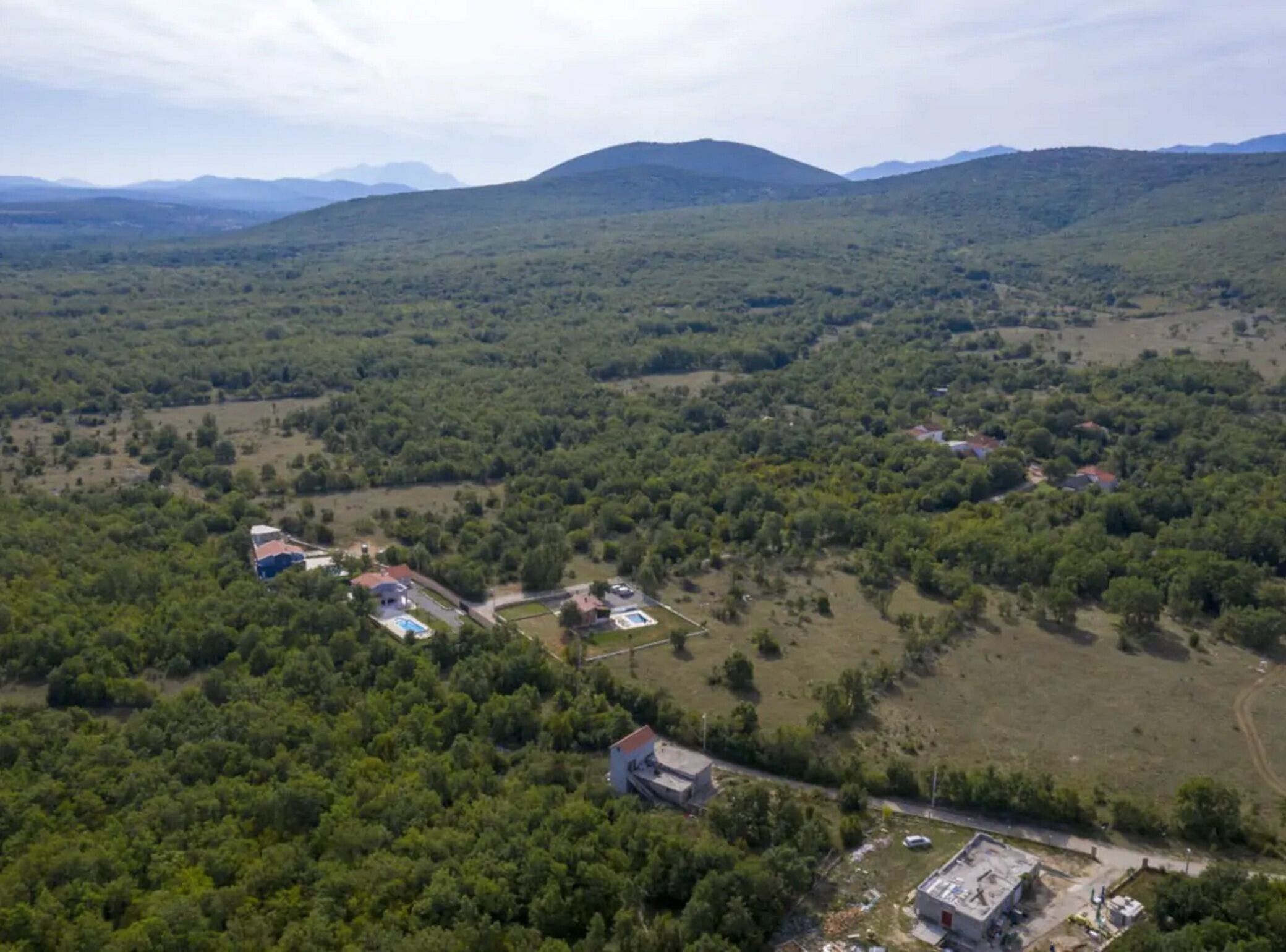 An aerial view of a rural area with scattered buildings, including houses and a small complex with a swimming pool.
