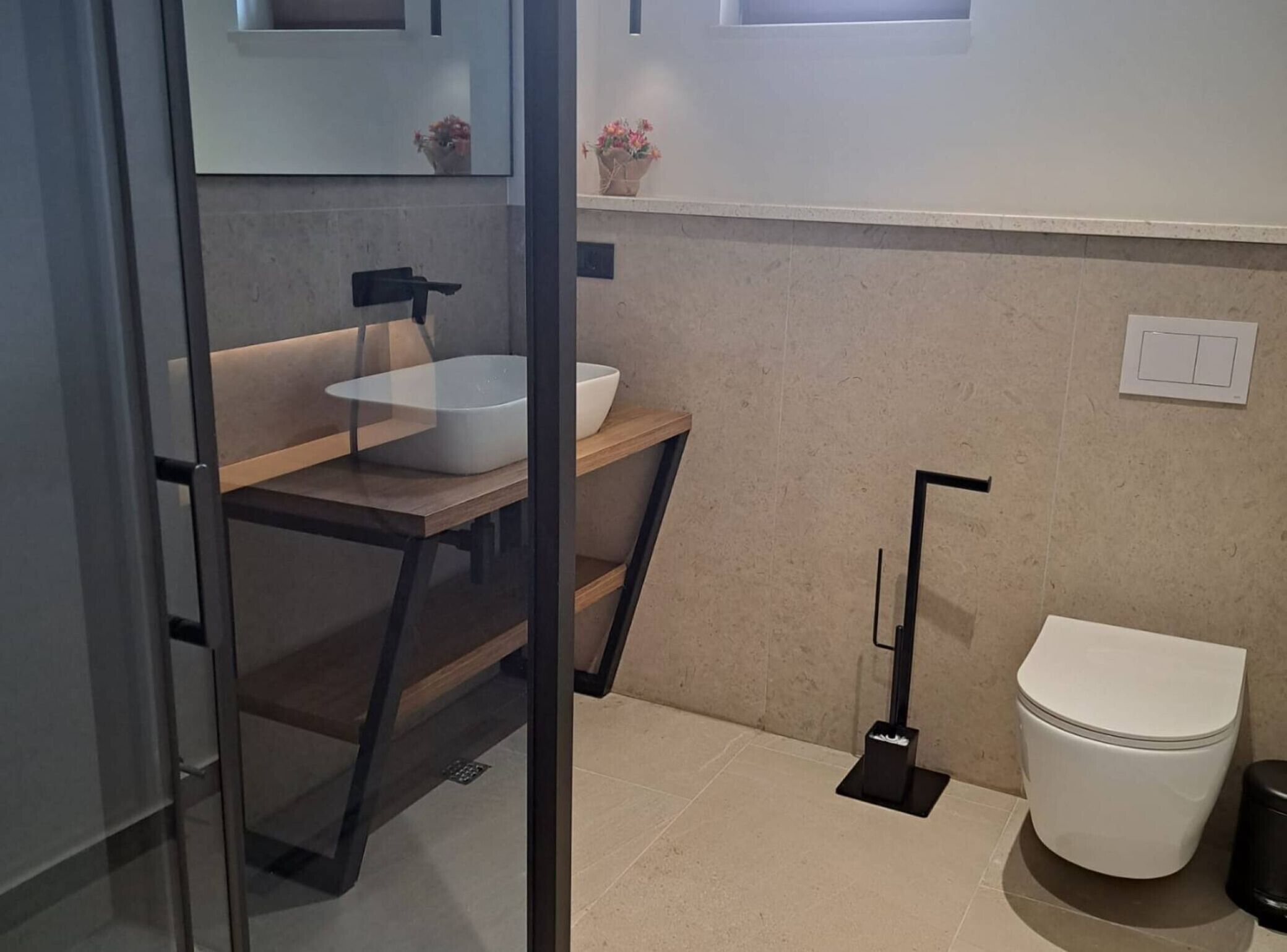 A modern bathroom with a glass partition, a white sink, a toilet, and a small window.