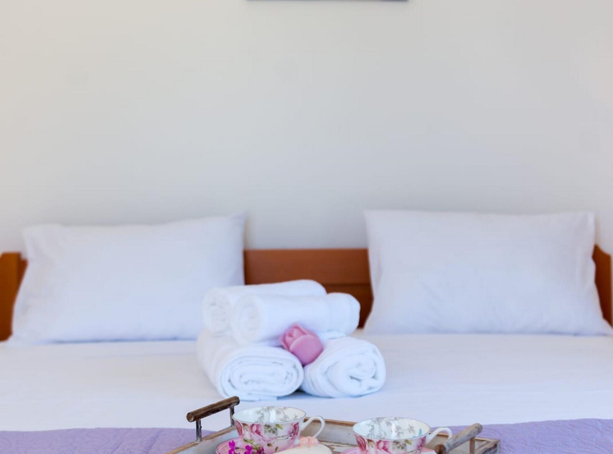 A neatly made bed with white linens, a wooden headboard, and a tray with a teapot and cups.