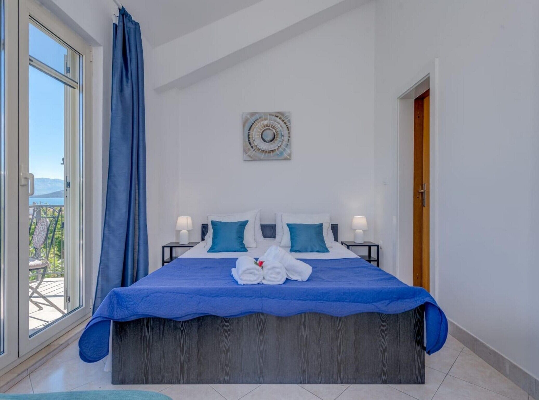 A bedroom with a large bed, two bedside tables, a window with a view, and a door.