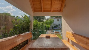 A wooden table with benches in a covered outdoor area with a view of a swimming pool and a house in the background. - Four Bedroom Holiday Home with Pool and Gym (Dicmo Kraj)
