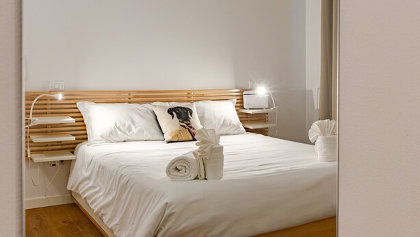 A neatly made bed with white linens, a wooden headboard, and a bedside lamp.
