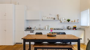 A modern kitchen with white cabinets, a wooden dining table, and a built-in stove.