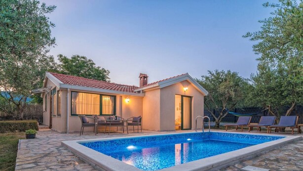 Une maison avec une piscine, une terrasse en pierre et du mobilier d’extérieur.